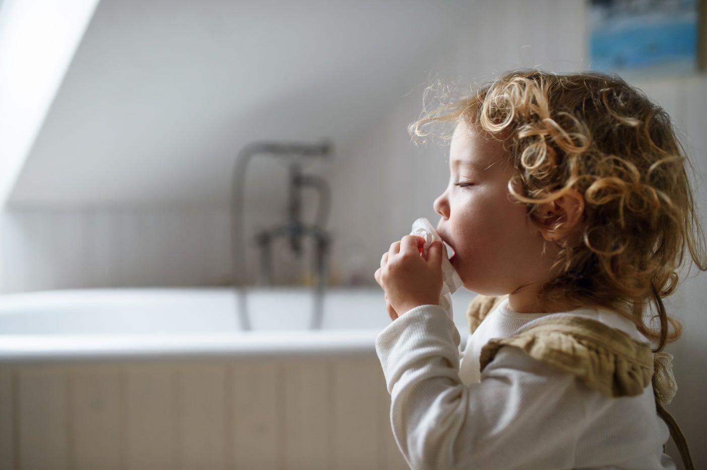 A toddler with walking pneumonia coughs into a tissue