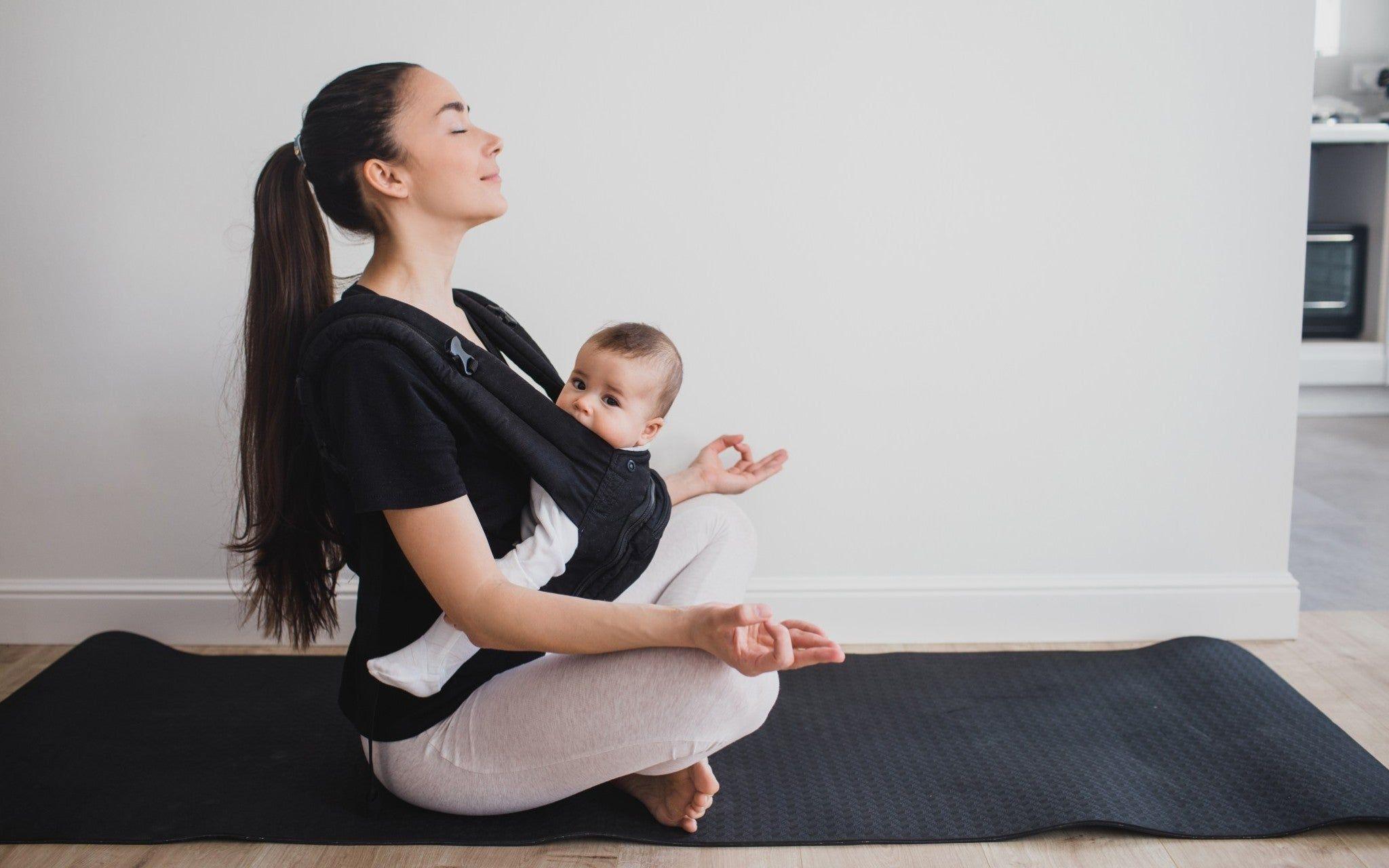 Mum practicing yoga while wearing her baby in a carrier