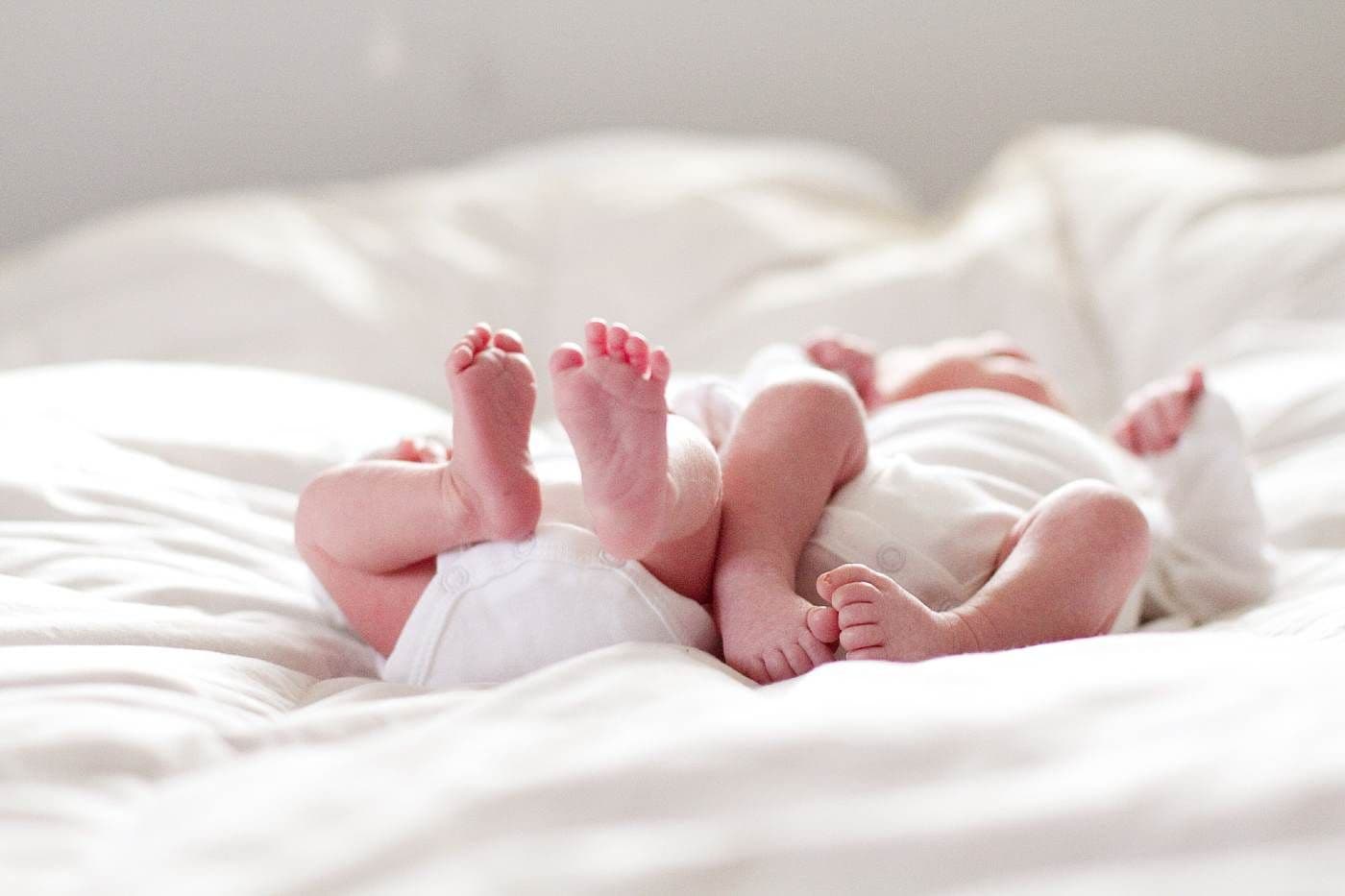 Twin babies laying on a bed.