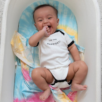 Baby in 'I'm the Happiest!' bodysuit in SNOO bassinet with Rainbow Tie-Dye SNOO Sheet and Rainbow Tie-Dye SNOO Sack