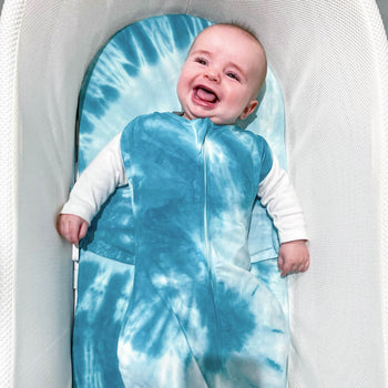 Happy baby in Blue Tie-Dye SNOO Sack with arms out on Blue Tie-Dye SNOO Sheet in SNOO bassinet